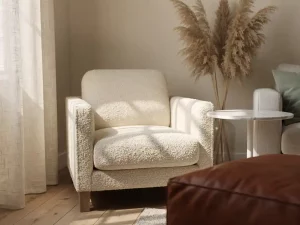 Ivoren bouclé fauteuil in Nederlandse woonkamer met marmeren bijzettafel, pampasgras en linnen gordijn in middaglicht.