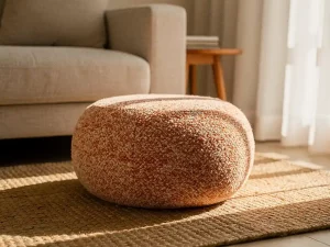 Ronde bouclé poef in zand- en terracottatinten op een juten vloerkleed, met linnen bank en houten bijzettafel in warm middaglicht.