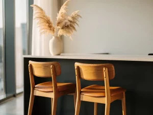 Natuurlijke eiken barkrukken met leren zitting aan strakke receptiebalie, warm ochtendlicht en pampasgras in minimalistische vaas.