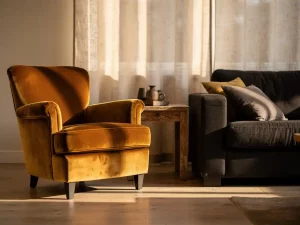 Caramel fluwelen fauteuil naast een houtskoolgrijs sofa in een Nederlandse woonkamer, met zacht natuurlijk licht door linnen gordijnen.