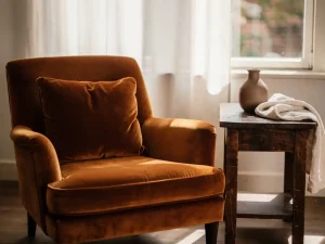 Cognac fluwelen fauteuil naast rustiek houten bijzettafeltje met keramische vaas en linnen plaid, zacht middaglicht in Nederlandse woonkamer.