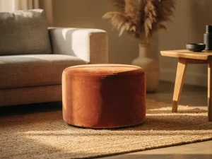 Ronde terracotta velvet pouf op een naturel jute vloerkleed, omringd door een linnen bank, eiken bijzettafel en pampasgras in keramieken vaas.