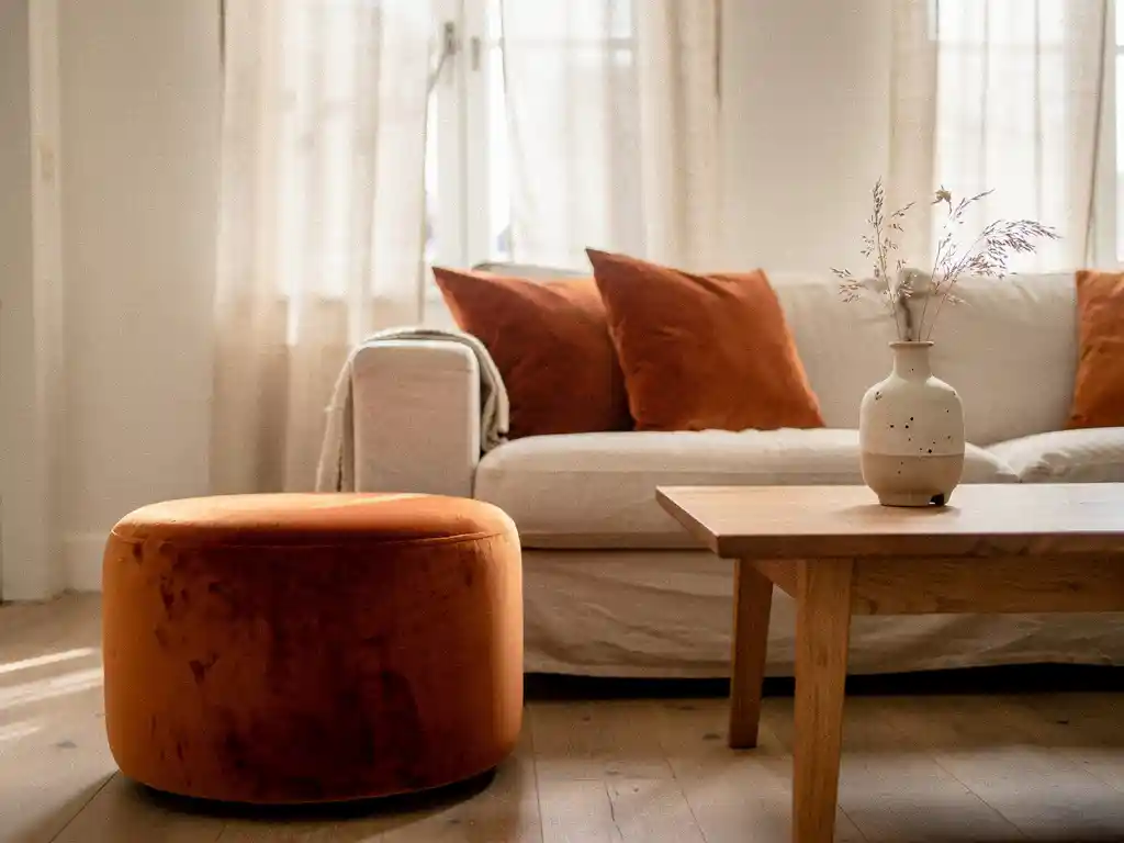 Terracotta fluwelen poef naast een linnen bank in een lichte Nederlandse woonkamer met eikenhouten salontafel en keramische vaas.