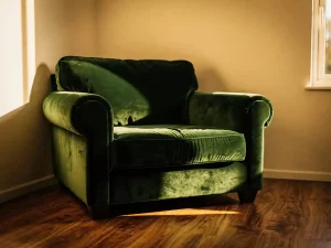 Overmaatse fauteuil in donkergroen fluweel in kleine woonkamer met crèmekleurige muren en walnoothouten vloer.