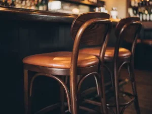 Drie houten barkrukken met lederen zitting langs een donkere eiken bartafel in een sfeervolle bar met warm amberkleurig licht.