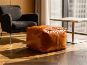 Cognac leren pouf op visgraatparket in een stijlvolle corporate lounge met marmeren bijzettafel en wollen fauteuil.