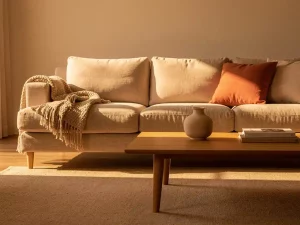 Linnen bank met diepe kussens en houten poten in warme woonkamer met terracotta tinten, geweven plaid en keramieken vaas.