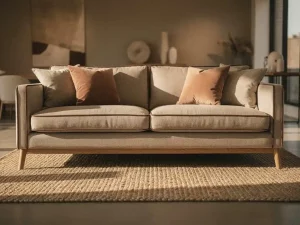 Linnen bank met natuurhouten poten en gelaagde aardetinten kussens op een gevlochten jutevloerkleed in een warmgelit interieur.