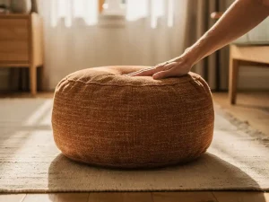 Ronde stoffen poef in terracotta en crème tinten op linnen vloerkleed, hand test stevigheid in gezellige Nederlandse woonkamer.