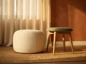 Ronde stoffen pouf en houten hocker op jute vloerkleed in Nederlandse woonkamer met linnen gordijnen en terracotta tinten.