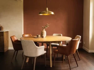 Ronde eiken eettafel met gemixte stoelen in linnen en cognackleurig leer, verlicht door hanglamp in warm Nederlands interieur.