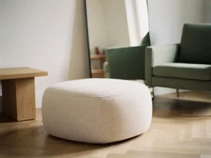 Ronde linnen poef op lichthouten visgraatparket in minimalistische woonkamerhoek met spiegel, saliegroen en warme crèmetinten.