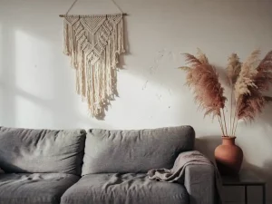 Verouderde woonkamerhoek met oversized grijze linnen bank, versleten macramé wanddecoratie en droog pampasgras in terracotta vaas.